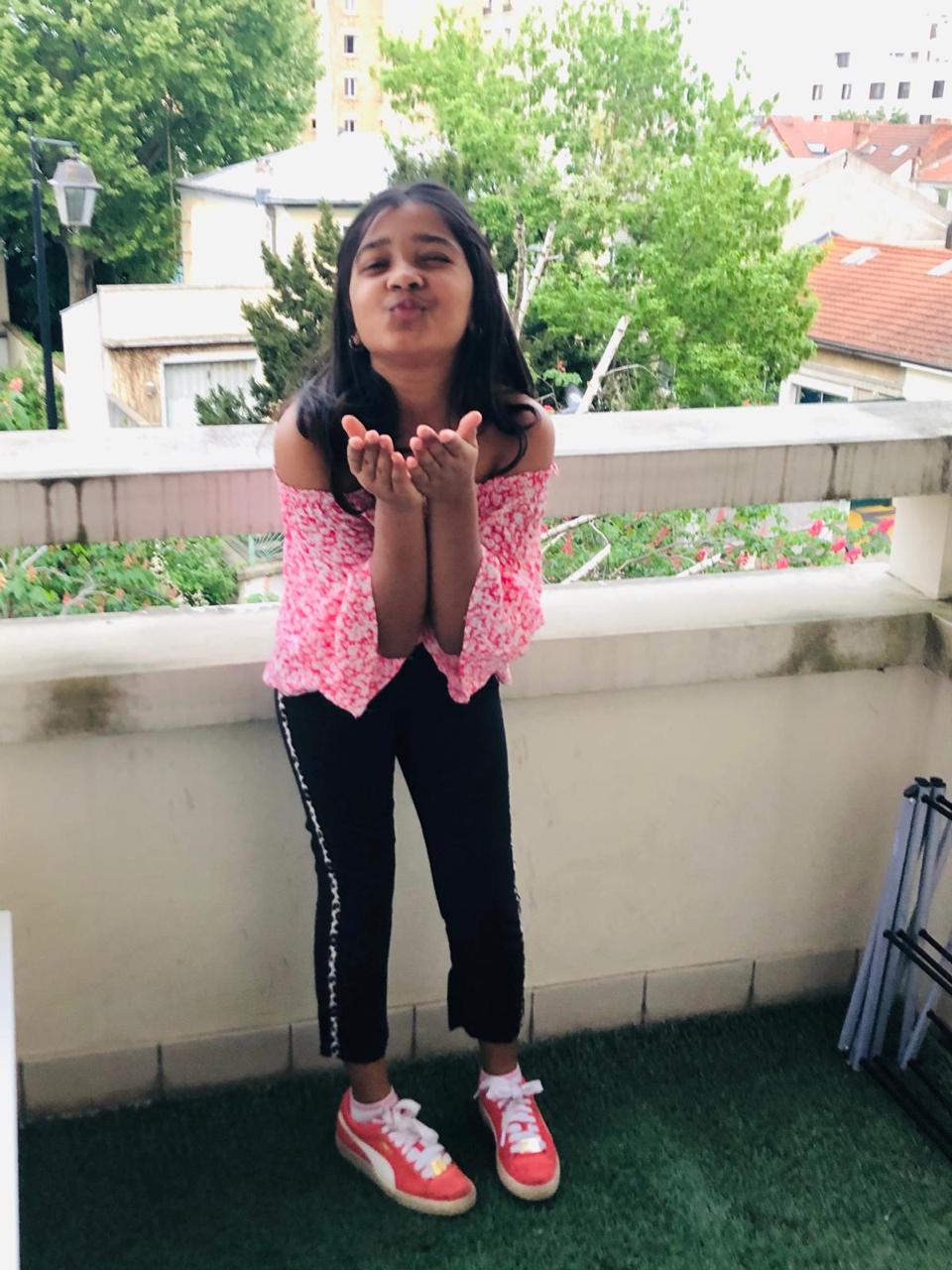 Young Anika on a balcony blowing a kiss at the camera