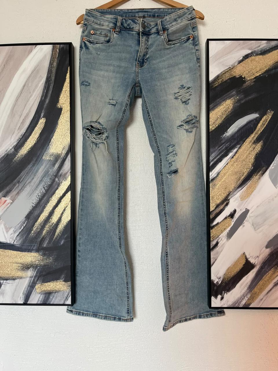 Light blue flared jeans, embroidered back pockets: "Inspired by the fear of being average" and "Make love, make art, make out"